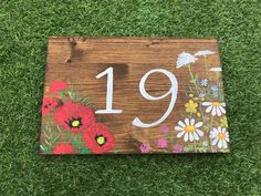 a wooden sign with flowers painted on it sitting in the grass next to some green grass