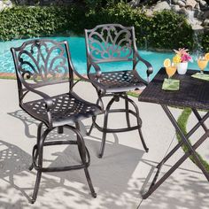 an outdoor table with two chairs next to a pool and flowers on the side walk