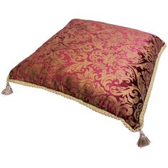 a pink and gold pillow with tassels on it's sides, sitting on a white surface