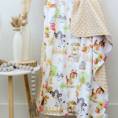 a baby's blanket with animals on it next to a white vase and wooden stool