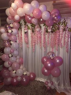 a bunch of balloons that are hanging on a wall in front of a curtain with pink flowers