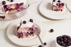 blueberry cheesecake on two white plates with spoons and bowl of berries next to it