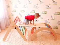 a small child playing on a wooden bench in a room with wallpaper and curtains