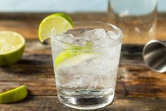 a glass filled with ice and lime on top of a wooden table