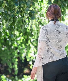 a woman standing in front of trees with her back to the camera, wearing a white sweater and black pants