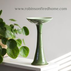 a green vase sitting on top of a white table next to a potted plant