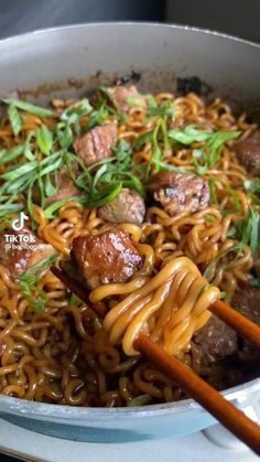 some noodles and meat are being cooked in a pan with chopsticks on the side