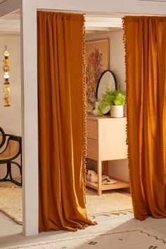 an orange curtain is open to reveal a room with a mirror and plant in it