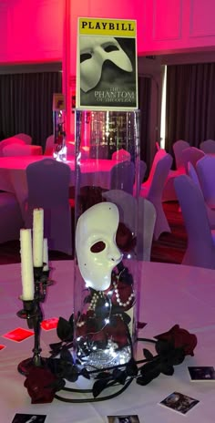 a white mask in a vase with roses and candles on a table at a party