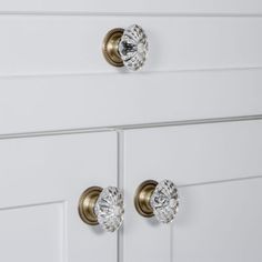 two knobs on the front of a white cabinet with brass handles and glass knobs