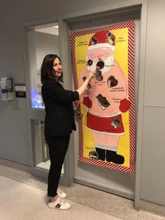 a woman is standing in front of a poster with santa clause on it and pointing to the side