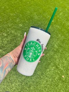 a woman holding a starbucks cup with a green straw in her hand on the grass