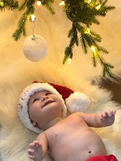 a baby wearing a santa hat laying under a christmas tree