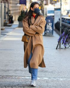 a woman walking down the street with her face mask covering her mouth and wearing a coat