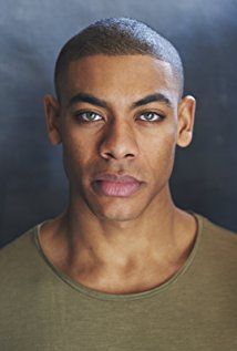 a close up of a person wearing a green shirt and looking at the camera with a serious look on his face