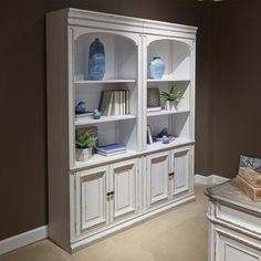 a white bookcase with blue vases and books on it in a living room