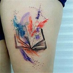 an open book tattoo on the back of a woman's thigh, with colorful ink splatters