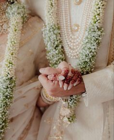 a man and woman dressed in white holding hands with flowers all around their necks