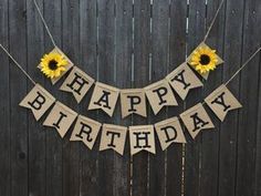 a happy birthday banner with sunflowers hanging from it's sides on a wooden fence