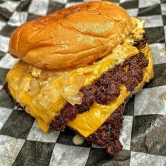 a cheeseburger on a checkered tablecloth with meat toppings and melted cheese