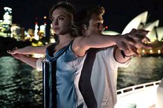 two people on a boat in front of the sydney opera house at night with their arms around each other