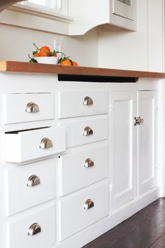 a kitchen with white cabinets and wood counter tops, an orange bowl on top of the cabinet