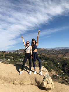 two young women standing on top of a mountain with their arms up in the air