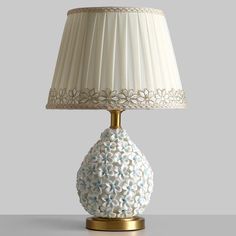 a white lamp with a gold base and blue flowers on the bottom is sitting on a table