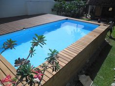 an empty pool in the middle of a backyard with wooden decking and plants around it