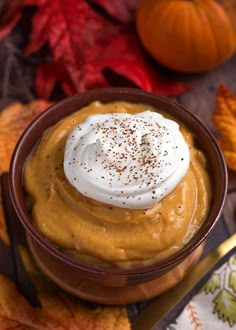 a bowl filled with whipped cream on top of a table next to autumn leaves and pumpkins