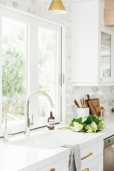 a white kitchen with marble counter tops and gold pulls on the faucet above the sink