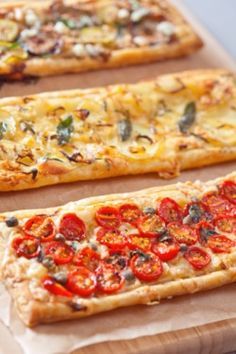 three slices of pizza with tomatoes on them sitting on top of a wooden cutting board