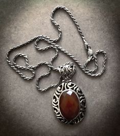 Indulge in luxury with our stunning and unusual 915 silver faceted large carnelian pendant, made in the 70s era in the Navajo Style and stamped with 925. It's accompanied by a 925 silver rope chain. This pendant necklace, featuring hand crafted scroll design, showcases the beautiful and timeless use of carnelian, a gemstone with a rich history dating back to the Bronze Age on the Isle of Crete. Known as the stone of courage, this pendant will instill confidence and strength in its wearer while also promoting calmness and focus. Own a piece of elegance and sophistication with our Faceted Large Carnelian Pendant Necklace. Dimensions: Pendant- 2"x 1"x. 25" Chain: 20" ITEMS ARE SOLD AS IS, NON-RETURNABLE WITH NO WARRANTY, ALL STONE WEIGHTS & GRADES HAVE BEEN ESTIMATED AND ARE APPROXIMATES. Elegant Carnelian Jewelry Stamped 925, Silver Carnelian Necklace With Large Pendant, Vintage Carnelian Engraved Jewelry, Oval Engraved Carnelian Jewelry, Elegant Engraved Carnelian Jewelry, Silver Carnelian Jewelry With Large Pendant, Vintage Sterling Silver Necklace With Large Stone, Vintage Silver Carnelian Necklaces, Vintage Silver Carnelian Necklace