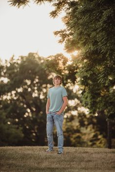 a young man standing on top of a grass covered field next to trees in the sun