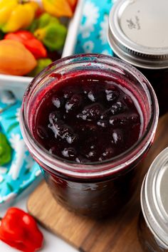 two jars of jam sitting on top of a wooden cutting board next to colorful peppers