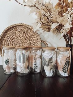 four glass jars with designs on them sitting on a table next to a basket and flowers