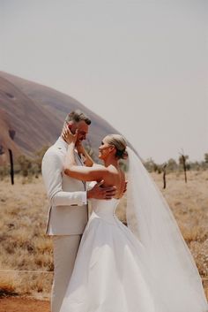 a bride and groom standing together in the desert