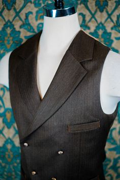 "ABOUT THIS STYLE: The style features a 1930s style jacket with a low gorge and a ticket pocket, a double-breasted notch collar vest, and a high-waisted pant with an extended waistband tab. With all of our designs, we look backward across the great history of menswear and try to bring forward is best and most fresh from the past, discarding what does not speak to our present age, but retaining all of the traditional craftsmanship and quaility. The suit is made from a vintage style herringbone su Formal Wool Vest With Notch Lapel, Classic Vest With Lapel Collar For Fall, Fitted Wool Vest With Notch Lapel, Brown Semi-formal Vest With Notch Lapel, Brown Notch Lapel Vest For Semi-formal Occasions, Fitted Brown Suit, Elegant Fitted Double-breasted Vest, Classic Three-piece Suit With Lapel Collar For Fall, Tailored Brown Vest With Notch Lapel