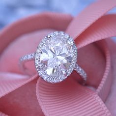 a diamond ring sitting on top of a pink satin ribbon with a bow around it