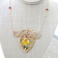 "The lemon quartz at the center of this necklace is bright, reminiscent of a midday sun. It isn't strictly a lemon quartz: there are little hints of orange to it. It glows rather magnificently. An exquisite frame of 14k gold fill wire has been constructed aroun the stone with complex swirls. A layer of chrome diopside, peridot, and tourmaline wraps around the inside and some madeira citrine accents the top of the stone. The pendant is about 2.5\" long by 3\" wide and the double layer chain is ad Citrine Gemstone Jewelry For May Birthstone, Green Citrine Jewelry Gift, Green Citrine Jewelry For Gifts, Elegant Yellow May Birthstone Jewelry, Green Citrine Jewelry With Gemstone Accents, Yellow Birthstone Pendant Jewelry, Peridot Jewelry With Gemstone Accents In Gold, Unique Citrine Gemstone Necklaces, Amber Citrine Necklace With Gemstone Accents