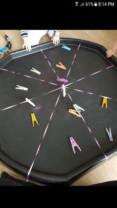 the child is playing with scissors on the black tray that was made from clothes pins