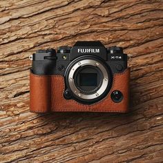 a camera sitting on top of a wooden table next to a brown leather case with the lens