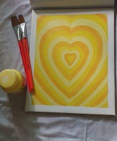 two paintbrushes are sitting next to a painting on a canvas with a heart