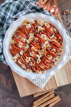 a bowl filled with carrots and nuts on top of a wooden cutting board next to cinnamon sticks