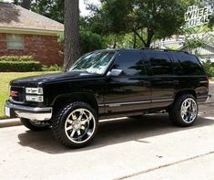 a black suv parked in front of a house on the side of the road with large tires and chrome rims