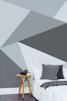 a white bed sitting next to a wall with grey and white designs on the walls