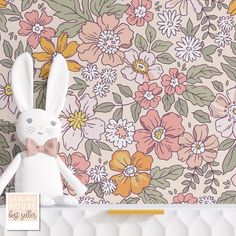 a white stuffed rabbit sitting on top of a shelf next to a wallpaper covered in flowers