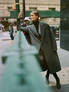 a woman leaning against a pole on the side of a street with her hand up in the air