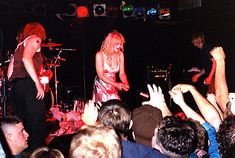 two women are performing on stage with their hands in the air as people look on