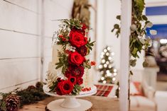 a three tiered cake with red flowers and greenery on the top is sitting on a table